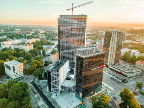 Aerial view of a modern cityscape featuring tall buildings under construction, surrounded by greenery and urban areas during sunset.