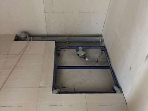 A rectangular construction area in a floor with exposed plumbing and framing edges.