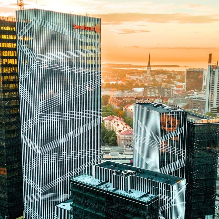 City skyline at sunset featuring modern high-rise buildings, including a prominent glass tower with a geometric pattern.