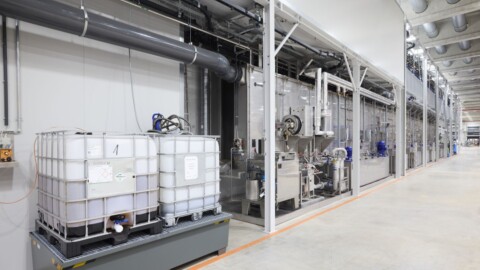 Industrial facility interior featuring large storage tanks and processing equipment arranged along a clean, spacious corridor.