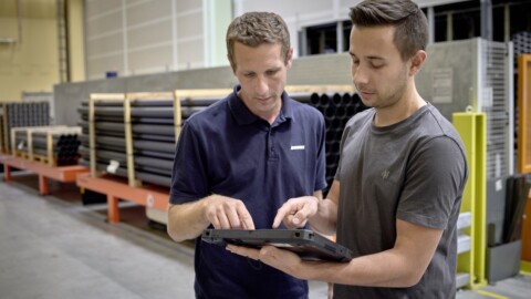 Zwei Personen in einem Lagerraum betrachten gemeinsam ein Tablet, während sie auf die Inhalte zeigen.