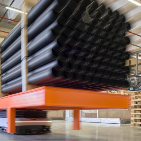 Ein kleines Fahrgerät hebt einen langen Metallträger, auf dem bis zu fünf Meter lange Rohre transportiert werden können.