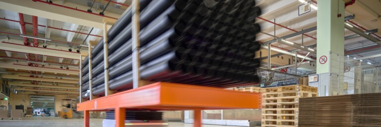 Ein kleines Fahrgerät hebt einen langen Metallträger, auf dem bis zu fünf Meter lange Rohre transportiert werden können.