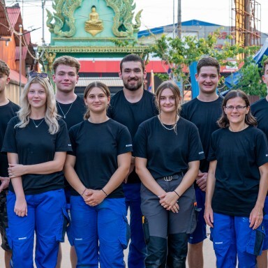 A group of twelve individuals in black shirts and blue pants posing together outdoors, smiling at the camera.