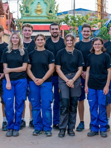 A group of twelve individuals in black shirts and blue pants posing together outdoors, smiling at the camera.