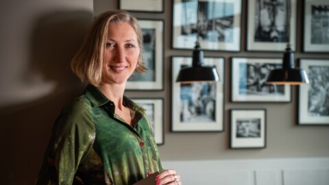 Frau mit schulterlangen Haaren steht in einem Raum mit Fotografien an der Wand.