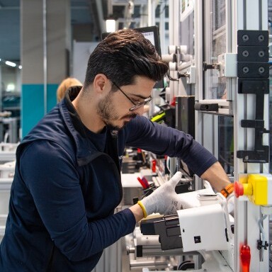 Ein Mann in Arbeitskleidung arbeitet an einem technischen Gerät in einem modernen Laborumfeld.