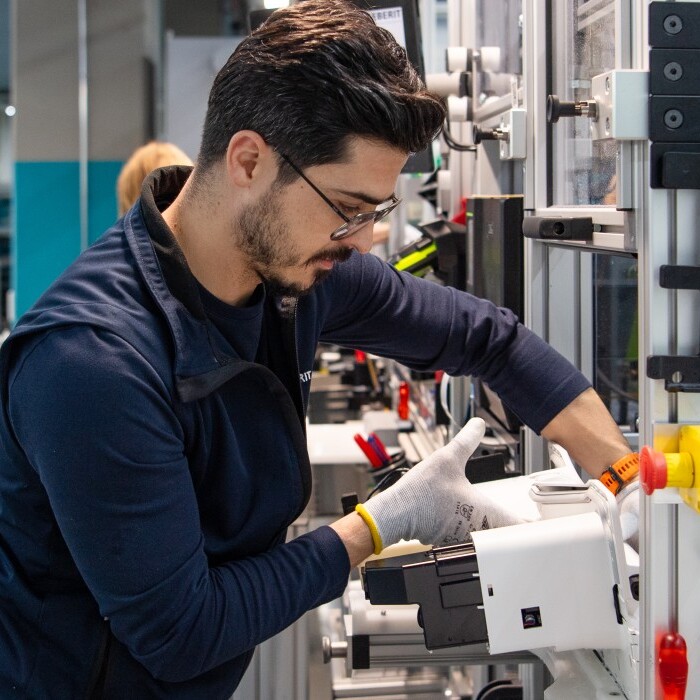 Ein Fabrikarbeiter in einem modernen Produktionsraum montiert ein Gerät mit einer präzisen Handbewegung.