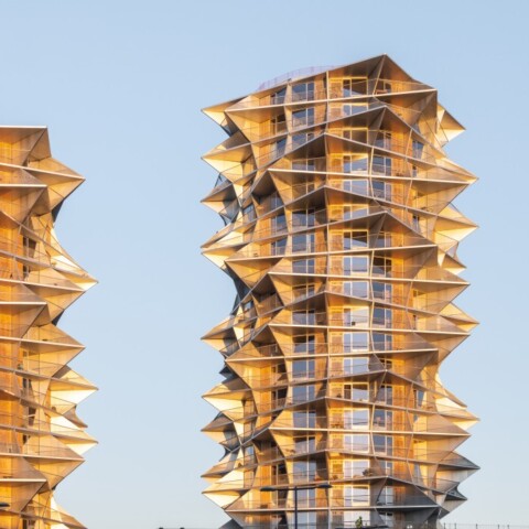 Zwei moderne Hochhäuser mit wellenförmiger Fassade und gläsernen Balkonen vor klarem Himmel.