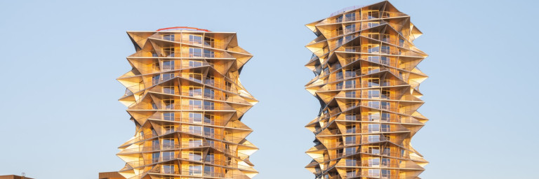 Zwei moderne Hochhäuser mit wellenförmiger Fassade und gläsernen Balkonen vor klarem Himmel.