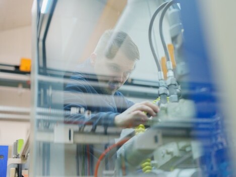 A technician working on machinery with various tubes and control valves in a workshop setting.