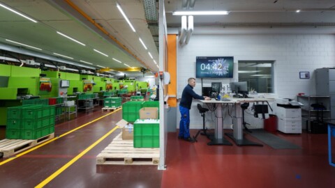 A manufacturing facility with green machines on the left and a workstation with a monitor displaying the time on the right.