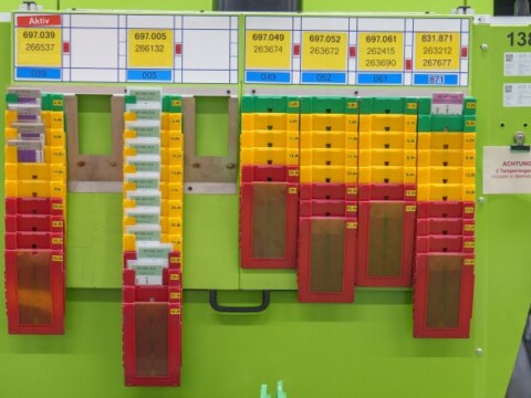 A board with various colored bins and labels, displaying organized items and data, set against a green background.