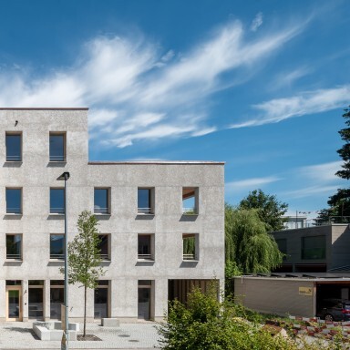 Ein modernes, mehrstöckiges Gebäude mit Betonfassade, Fenstern und umgebender Grünfläche unter einem blauen Himmel.