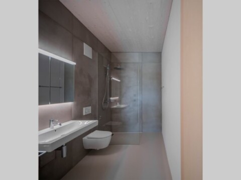 Modernes Badezimmer mit grauen Wänden, einer gläsernen Duschkabine, Waschbecken und WC.