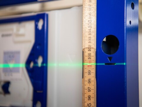 Ein blauer Rahmen mit einem Laserstrahl in grüner Farbe, neben einem Zollstock, der zur Messung verwendet wird.