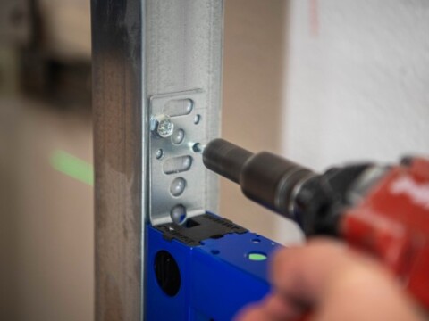 Eine Hand hält einen Akku-Schrauber, der Schrauben in eine metallene Struktur eindreht.