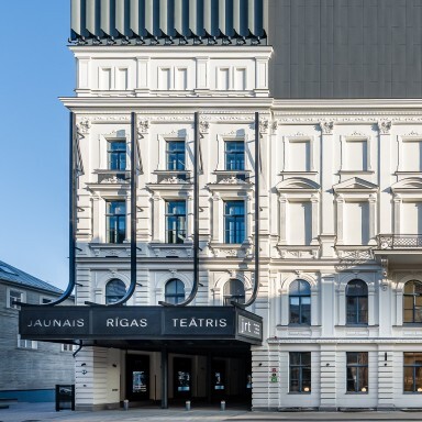 A modern theater building featuring a combination of classical white architecture with a contemporary black roof and distinctive signage.