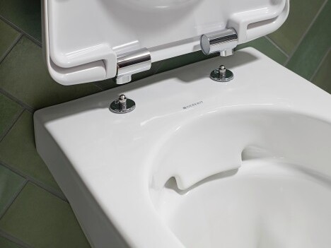 Close-up of a white toilet bowl with a raised lid, featuring chrome fittings.
