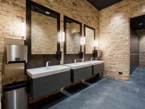 Modern restroom interior featuring three sinks with mirrors, stone walls, and a gray floor.