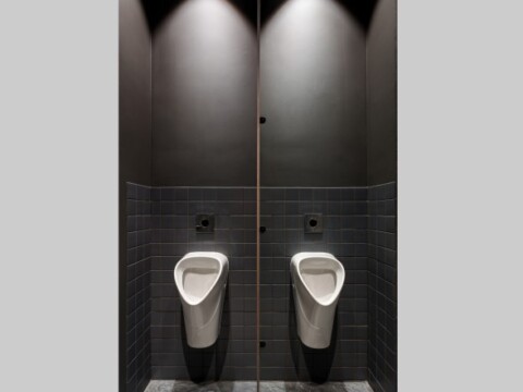 Two modern urinals placed side by side in a minimalist restroom, with dark walls and subtle overhead lighting.