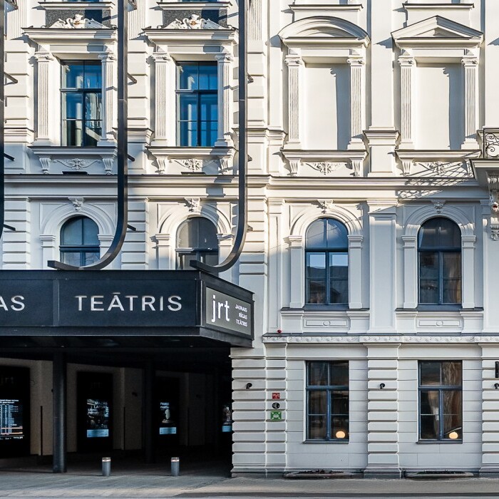 Theater building with a prominent black entrance sign reading "Jaunais Rīgas Teātris."