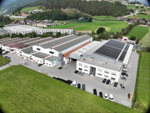 Eine grosse Industrieanlage mit mehreren Gebäuden, Solarzellen auf dem Dach und einer umliegenden Landschaft aus Wiesen und Bäumen.