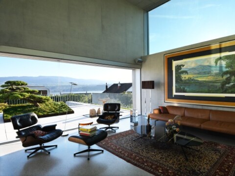 Contemporary living room with large windows, cozy seating, a decorative rug, and a view of outdoor greenery and mountains.