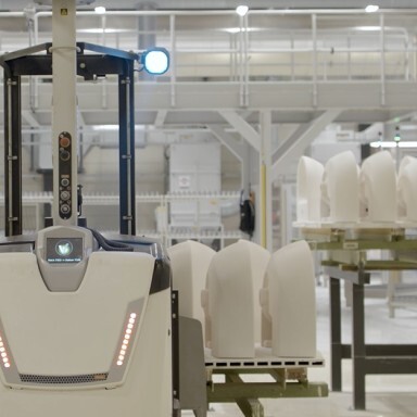 An automated robot in a manufacturing facility with white ceramics on a nearby shelf.