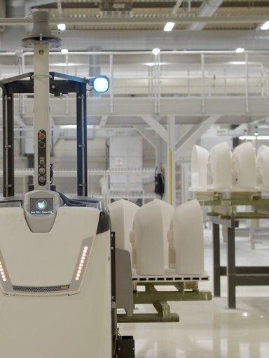 An automated robot in a manufacturing facility with white ceramics on a nearby shelf.