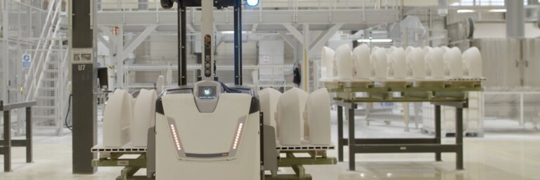 Autonomous industrial robot navigating in a warehouse with white ceramics on a cart in the background.