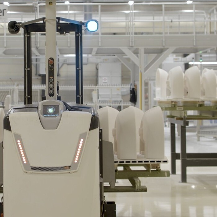 Autonomous industrial robot navigating in a warehouse with white ceramics on a cart in the background.