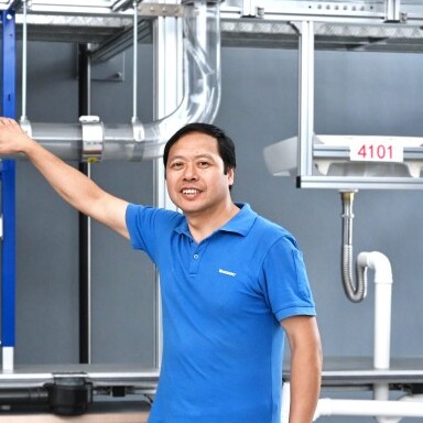 Ein Mann in einem blauen Poloshirt steht vor einer technischen Anordnung von Rohren .