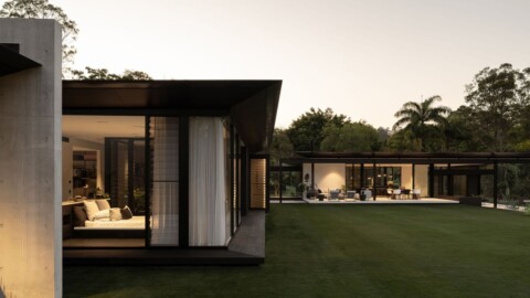 Moderne Architektur eines grossen Hauses mit grossflächigen Fenstern, umgeben von einem gepflegten Garten und Bäumen.