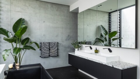 Modernes Badezimmer mit Betonwänden, grossen Pflanzen, einem eleganten Waschbecken und Spiegeln.