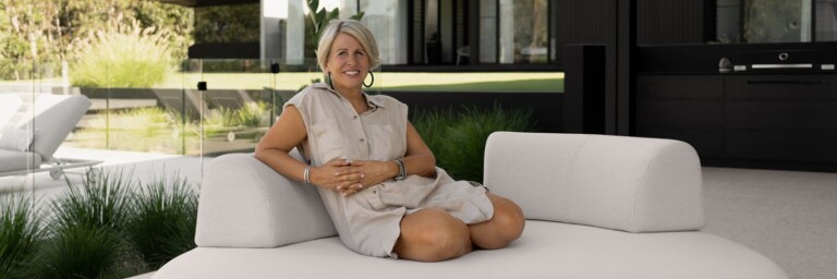 Eine Person sitzt im Freien auf einem modernen, hellen Sofa, umgeben von Pflanzen und einem zeitgenössischen Gebäude.