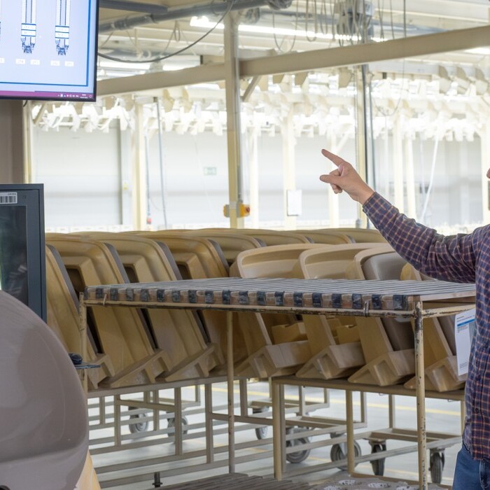 Eine Person in einem Fabrikraum zeigt auf einen Bildschirm mit Datenvisualisierungen.