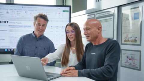 Three professionals collaborating around a laptop in an office setting.