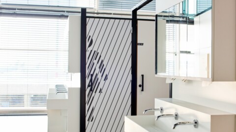 Moderne Badezimmeransicht mit einem eleganten Waschbecken, Spiegel und einer halbtransparenten Tür mit Linienmuster.