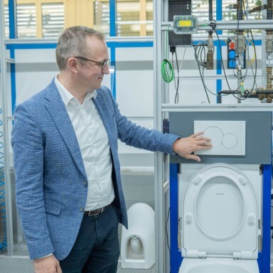 A man in a blazer interacts with a toilet flushing mechanism in a technical facility.