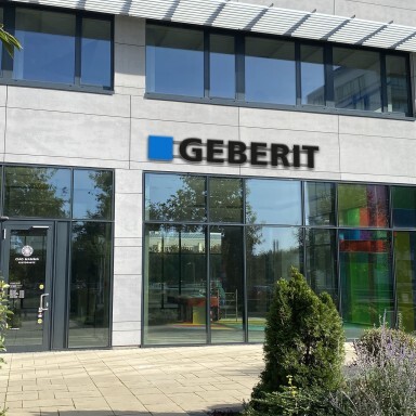 Modern building exterior with large windows, Geberit signage, and landscaped greenery.
