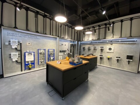 A modern exhibition space featuring plumbing equipment displays on the walls, with a central wooden table showcasing additional fixtures and tools.