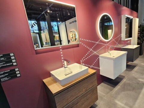 A modern display of bathroom vanities featuring sinks, various mirrors, and a striking burgundy wall.