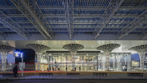 Moderne Gebäude mit Glasfront und abstrakten Säulen, beleuchtet bei Nacht.