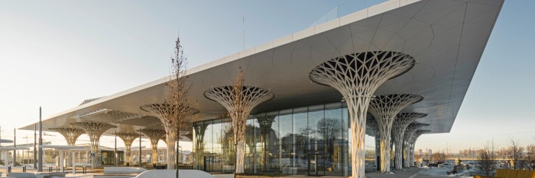 Moderne Architektur eines Gebäudes mit einem grossflächigen Dach, das auf baumähnlichen Stützen ruht, umgeben von Schnee.