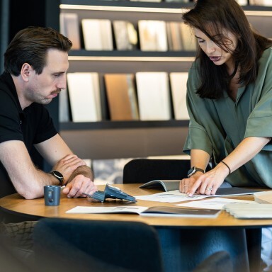 Ein Mann und eine Frau arbeiten gemeinsam an einem Tisch mit Dokumenten und Materialien in einem modernen Raum.