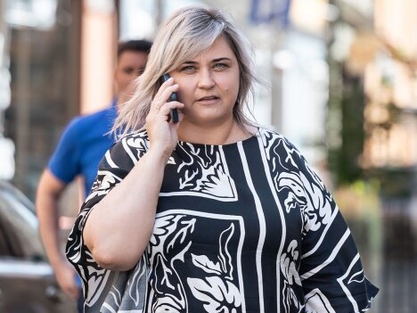 A woman  wearing a black and white patterned shirt, talking on a smartphone while walking on a street.