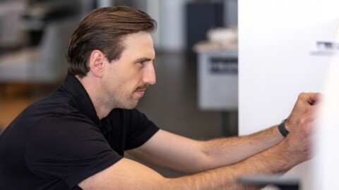 A man in a black shirt is focused on adjusting a device or appliance while seated in a modern indoor setting.