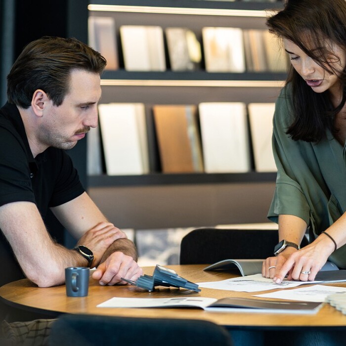 Two people discussing and analyzing documents at a table, with design samples visible in the background.