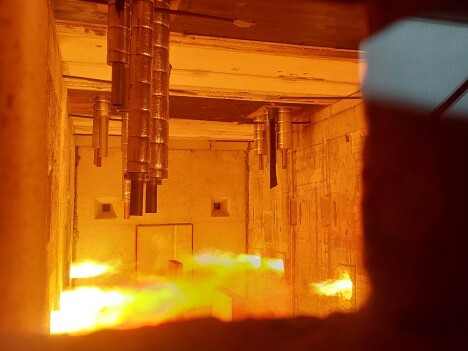 A dimly lit industrial setting with flames and pipes visible on the ceiling, suggesting a high-temperature environment.